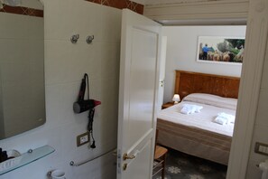 Habitación de hotel con ducha, cama con toallas, cabecero de madera y un cuadro enmarcado en la pared.