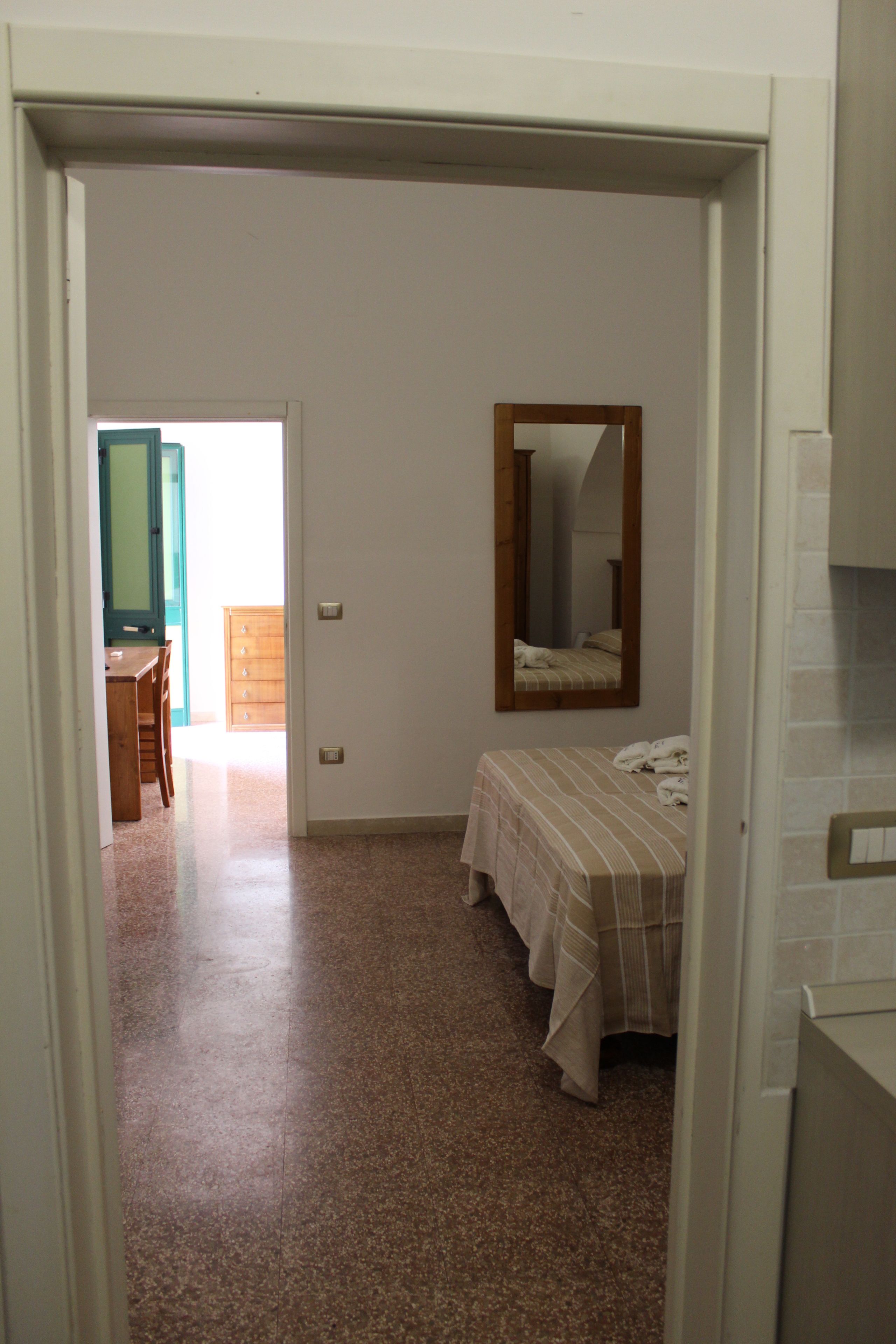 Un dormitori amb un llit, un taulell, un mirall i una porta que dona a una altra habitació.