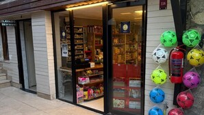 Un escaparate con puerta de cristal, estantes llenos de diversos artículos y balones de fútbol de colores exhibidos afuera.