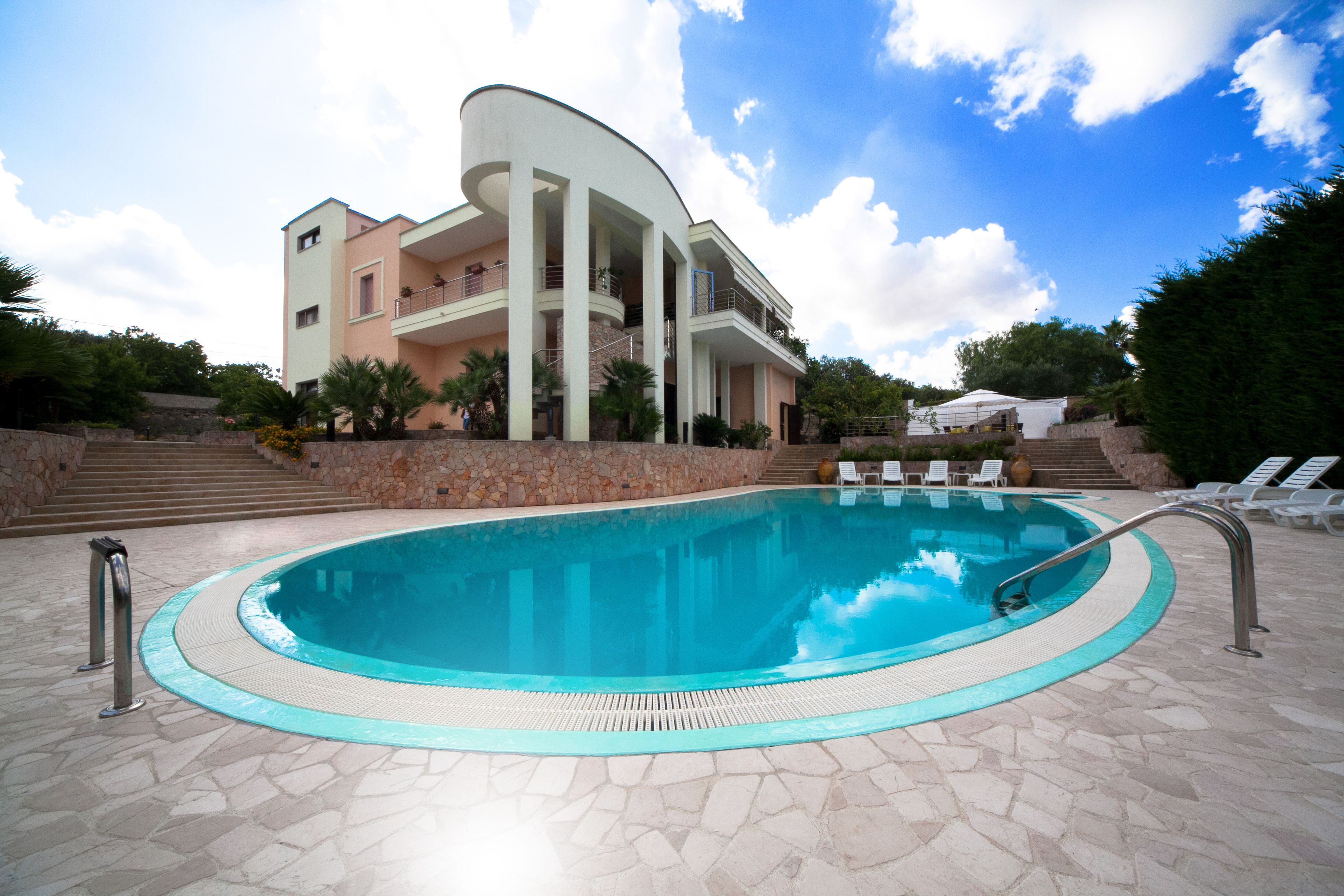 A swimming pool with a stone deck, a building with balconies, and a clear sky.
