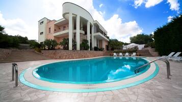 Una piscina con bordo in pietra, un edificio con balconi e cielo sereno.