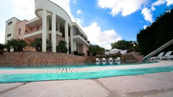 Un hotel moderno con piscina, un muro in pietra e un cielo azzurro intenso.