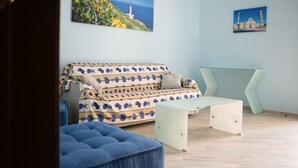 Un saló modern amb un sofà estampat, una taula de centre de vidre i un otoman blau.