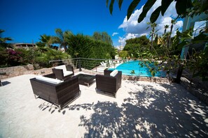 Ein Sitzbereich im Freien mit Korbmöbeln und einem Pool im Hintergrund.
