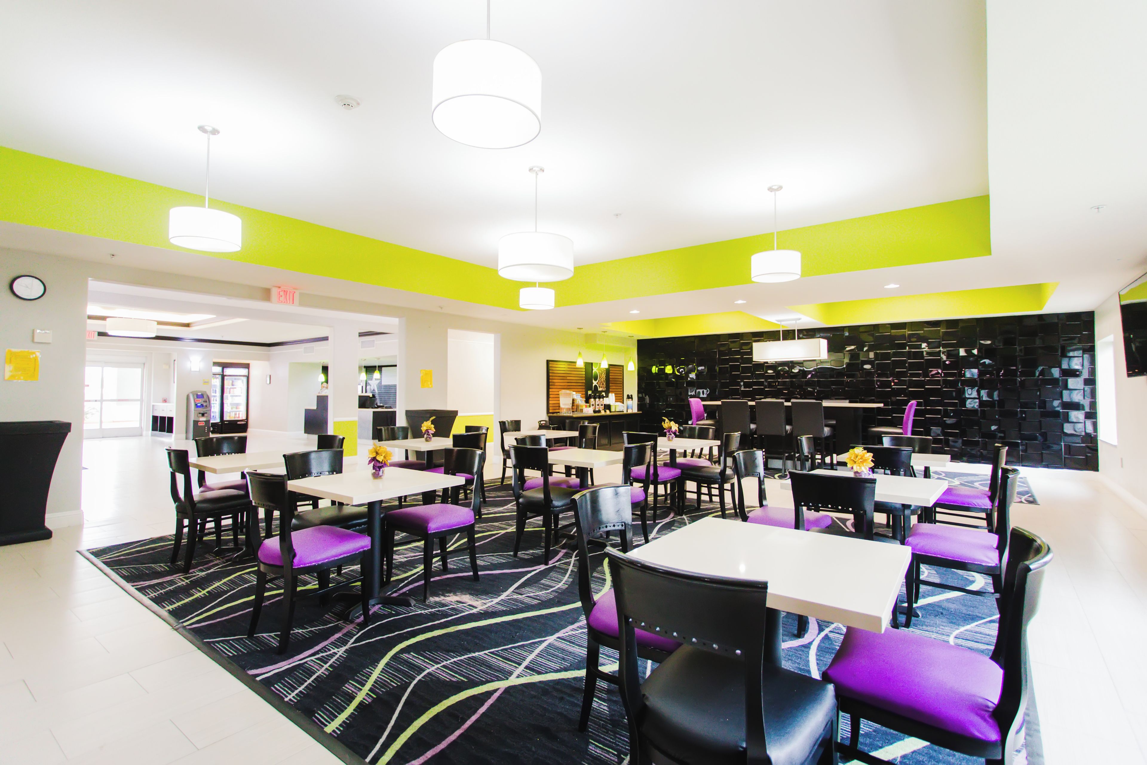 A modern dining area with tables and chairs, a patterned carpet, and a bright yellow accent wall.