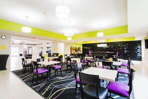 A modern dining area with tables and chairs, a patterned carpet, and a bright yellow accent wall. - Palacio Royale Inn Boutique Katy (Katy)