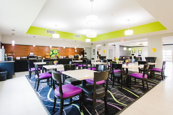 A modern dining area with multiple tables and chairs, a kitchen in the background, and a bright ceiling. - Palacio Royale Inn Boutique Katy (Katy)