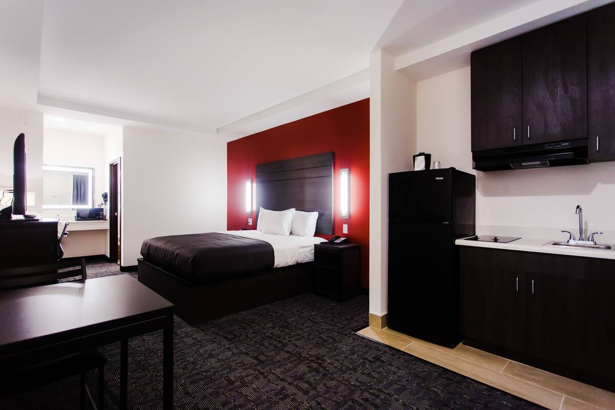 Una habitación de hotel con cama, mesita de noche, escritorio y un área de kitchenette.