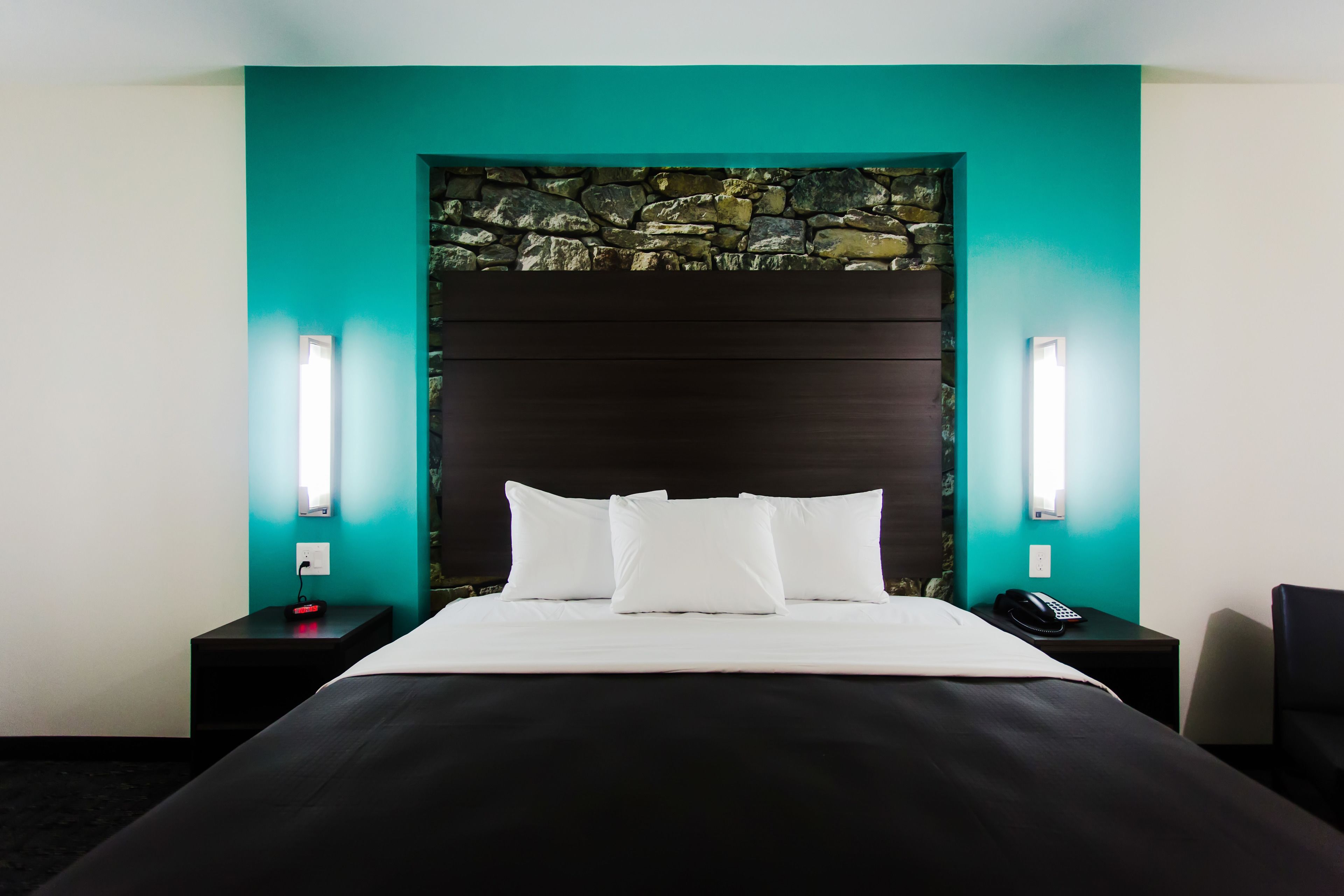 Une chambre d’hôtel avec un lit, un mur en pierre et deux tables de chevet avec des lampes.