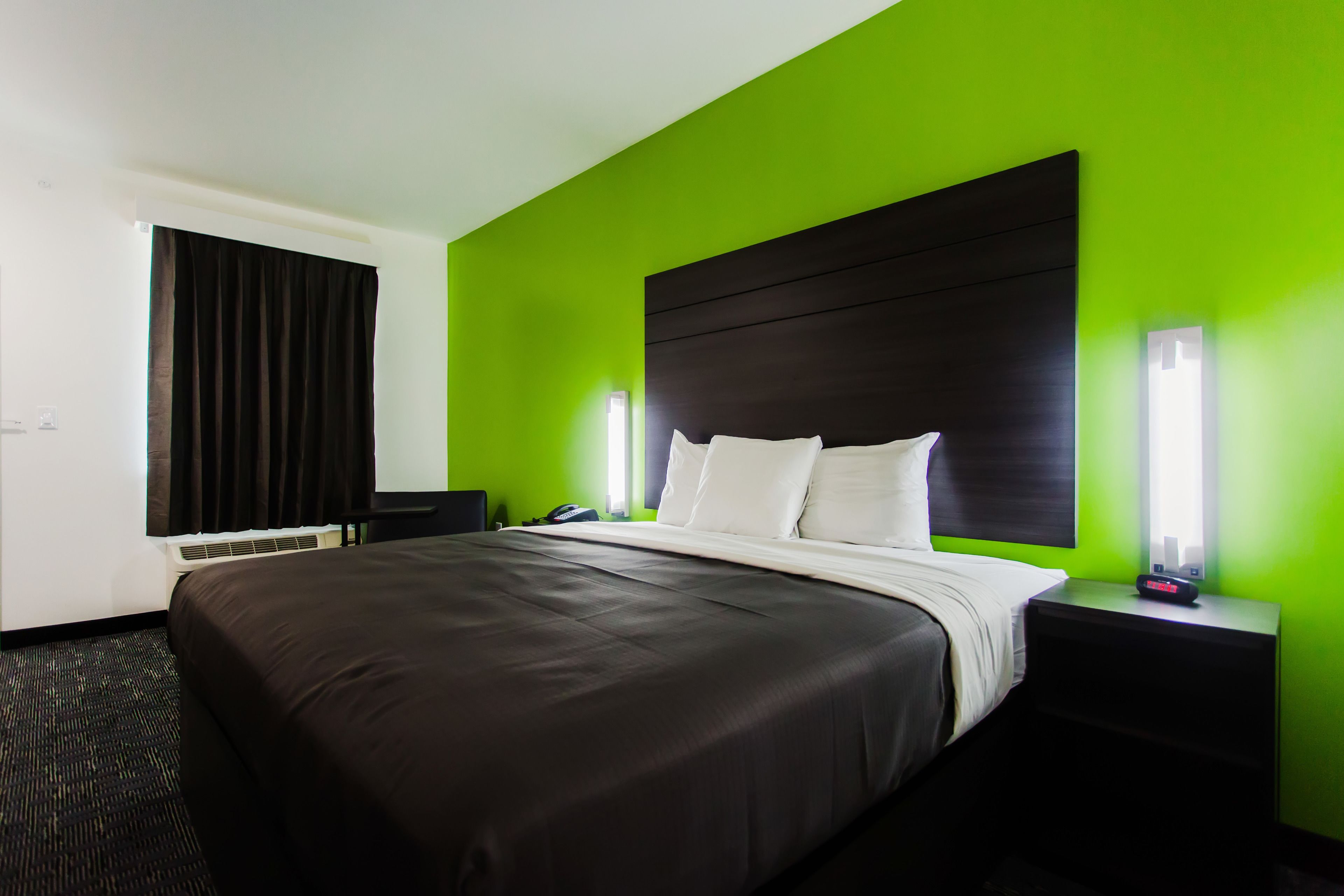 A hotel room with a large bed, a bedside table, a nightstand, a desk, and a window with curtains.