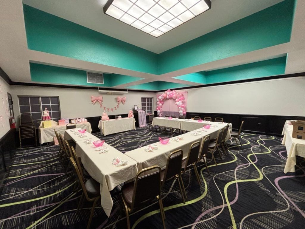 Un salón de conferencias con mesas y sillas, paredes color aguamarina y alfombra estampada.