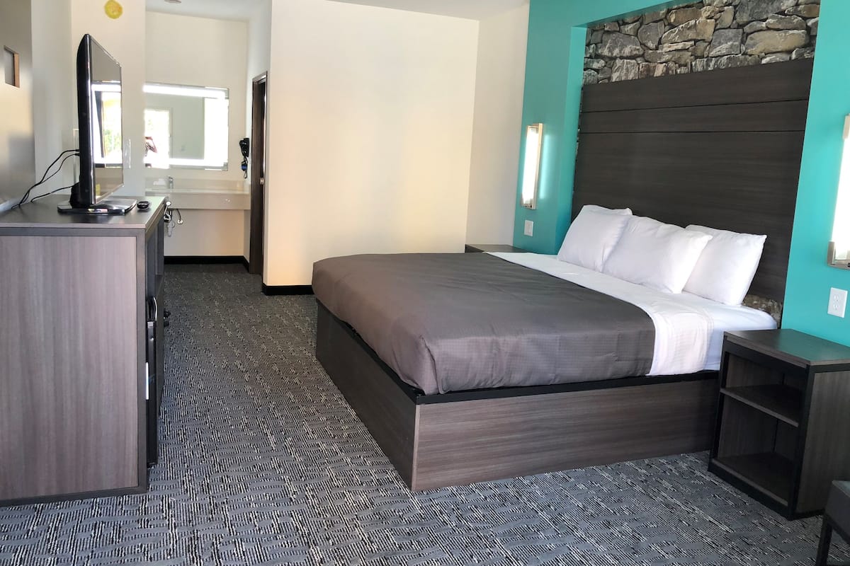 Una habitación de hotel con cama, escritorio, televisión y una pared de detalles de piedra.