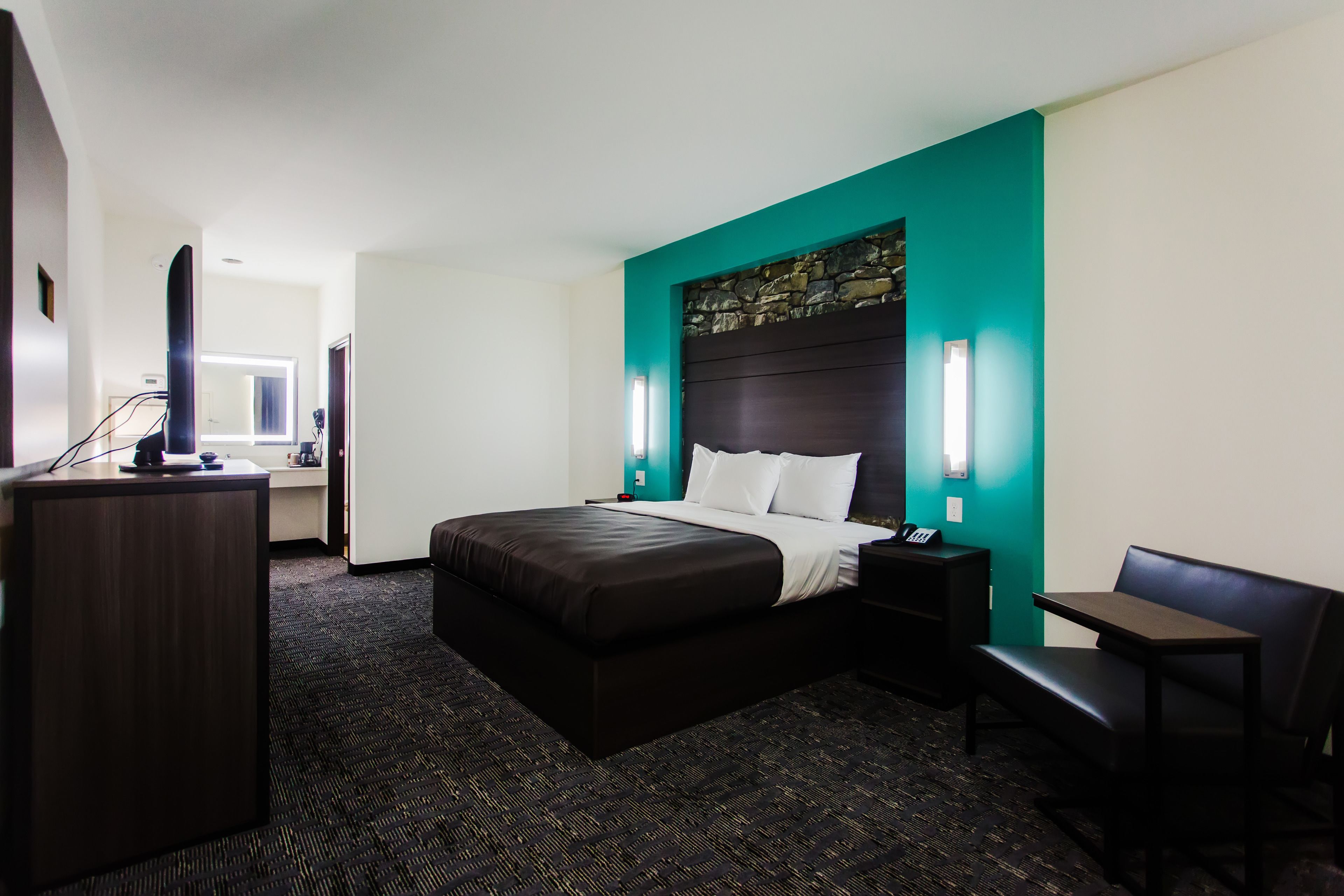 A hotel room with a large bed, a desk, a chair, and a TV.