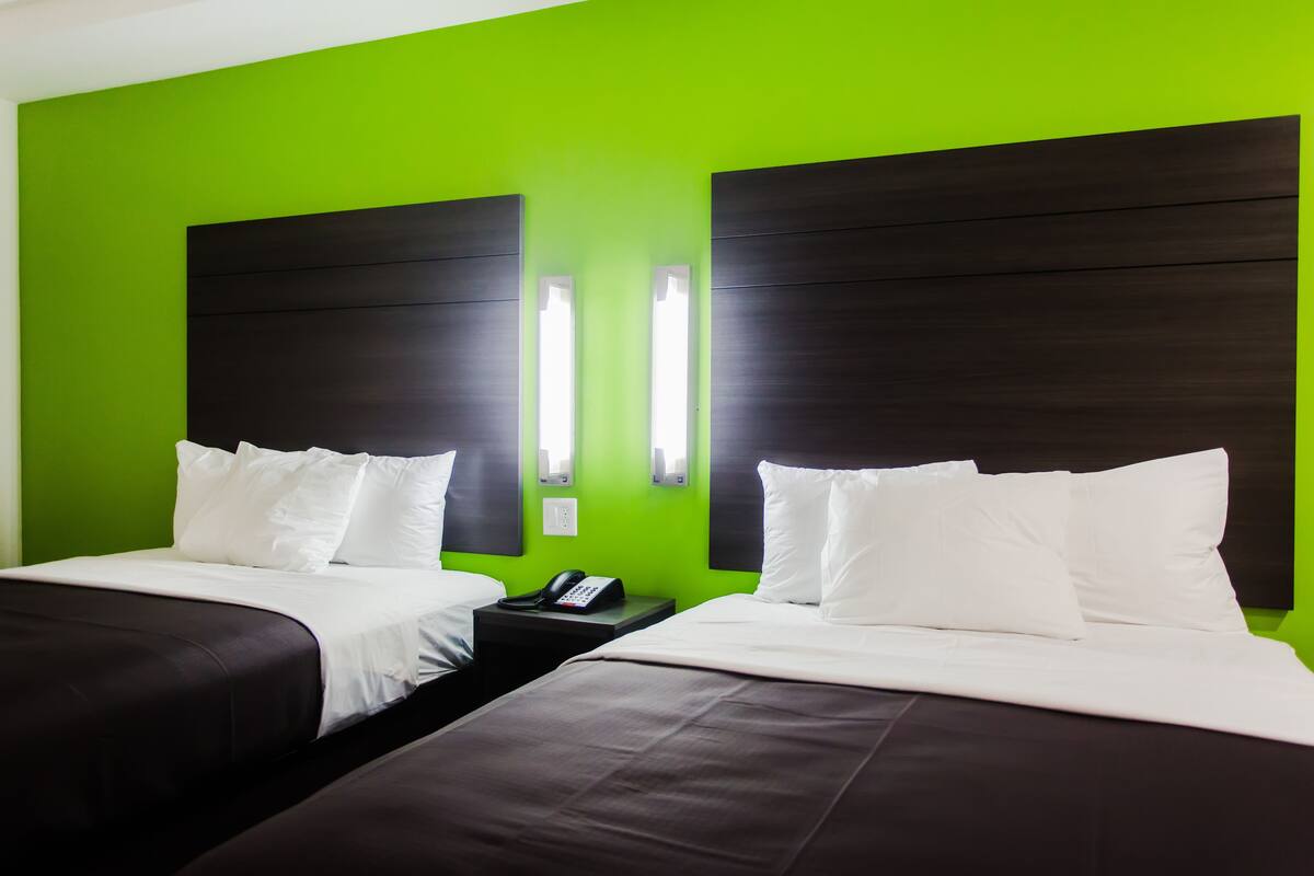 Una habitación de hotel con dos camas, paredes verdes y cabeceros de madera oscura.