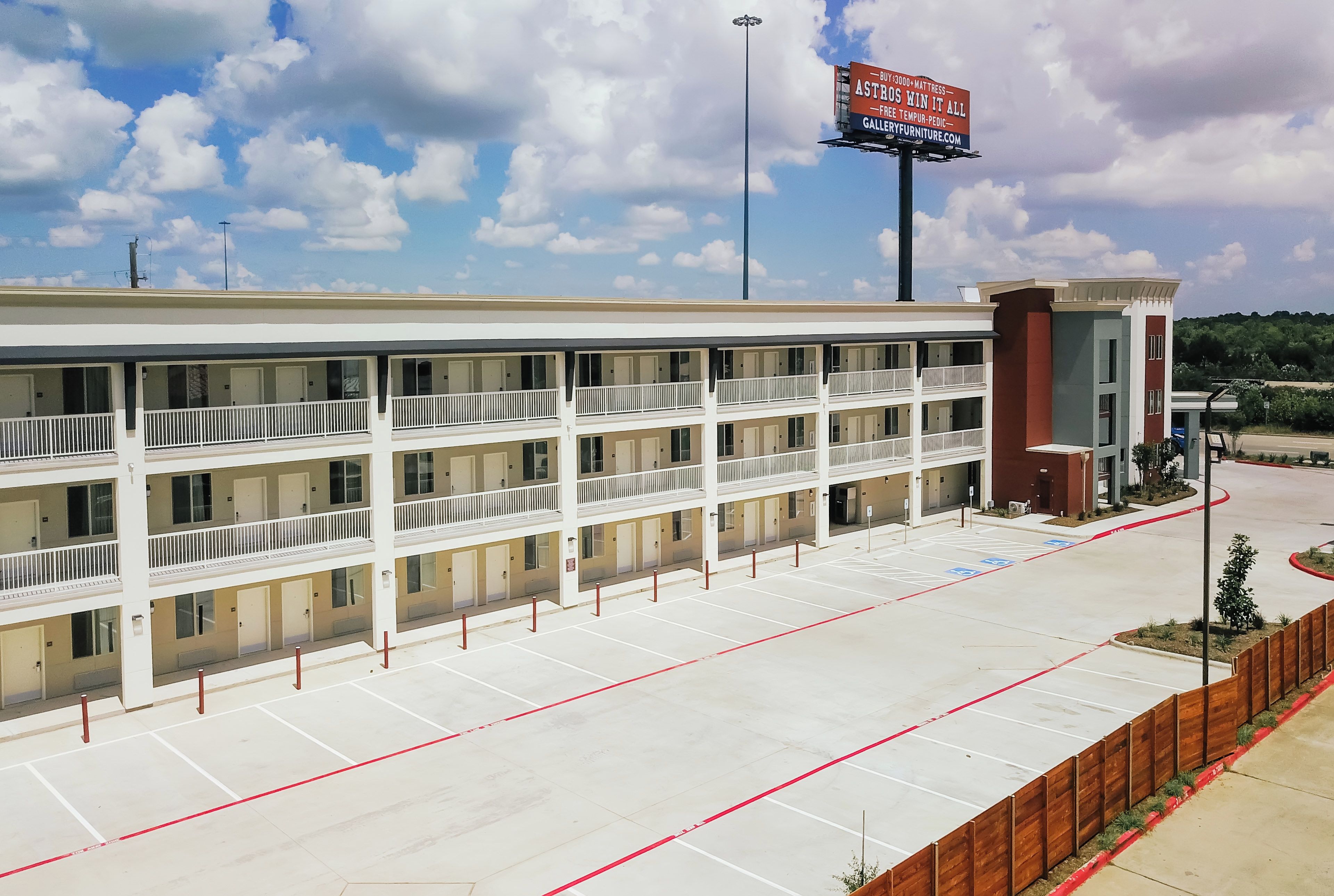 A multi-story hotel with a parking lot and a billboard advertising a mattress sale.