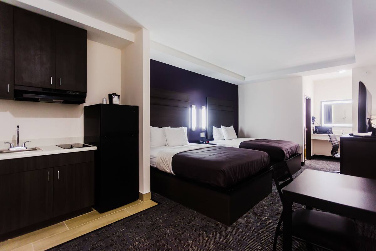 Habitación de hotel con kitchenette, dos camas, un escritorio y una silla.