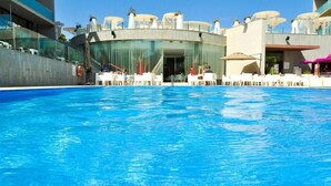 A swimming pool with a glass facade building in the background. - Aparthotel Four Elements Suites (Salou)