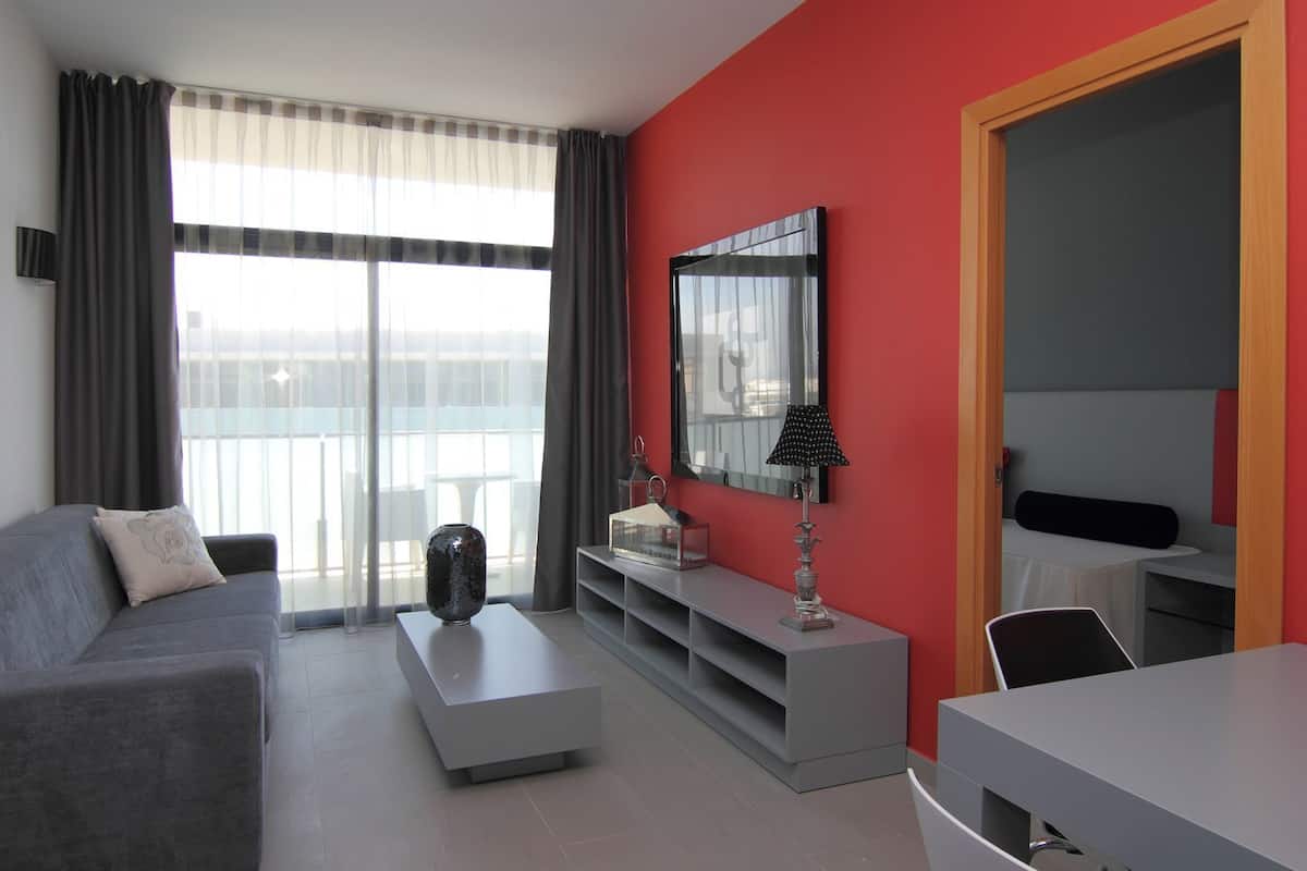 A modern living room with a grey sofa, a white coffee table, and a red accent wall.