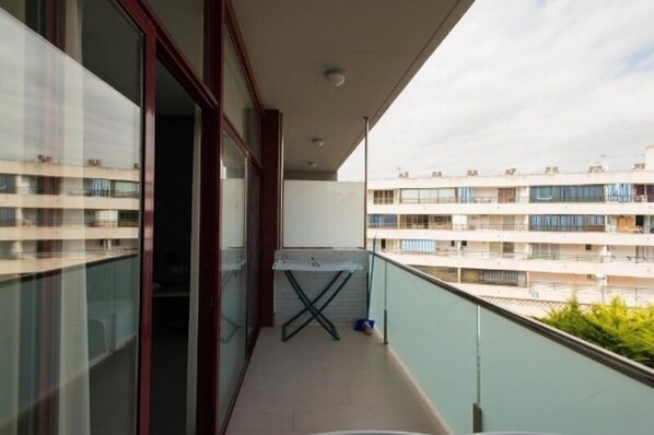 Varanda com mesa e cadeiras, vista para edifícios próximos e porta de acesso a um espaço interno.