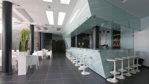 A modern bar area with a glass counter and white stools. - Aparthotel Four Elements Suites (Salou)