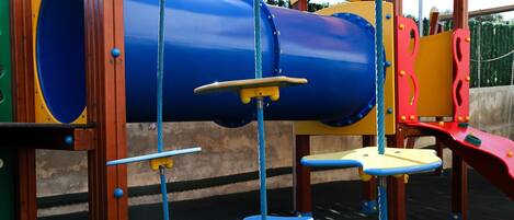 A playground with a blue cylindrical climbing structure, yellow and red play equipment, and a green slide.