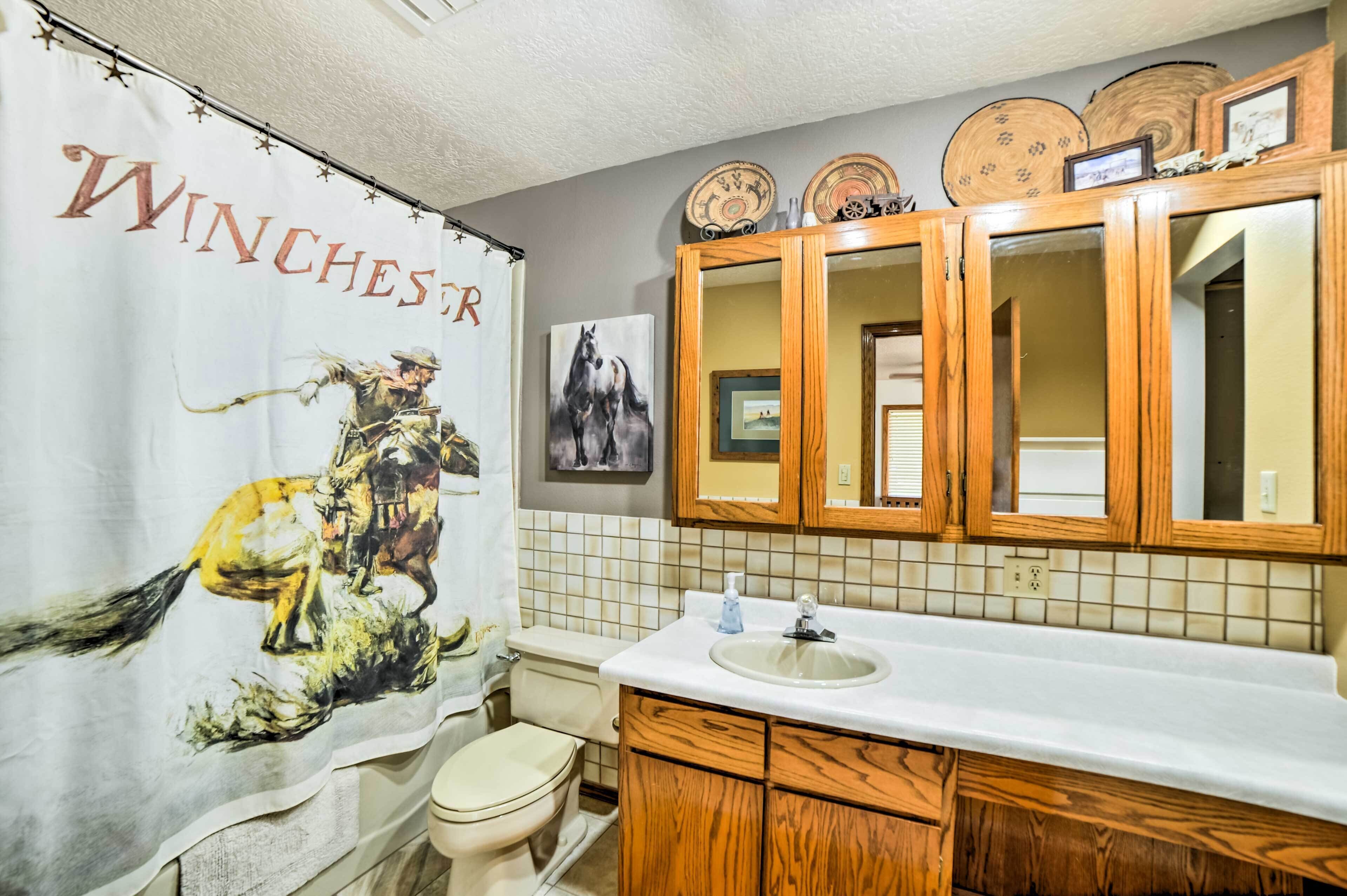 Un baño con cortina de ducha de temática occidental, armarios de madera, un lavabo y un espejo.
