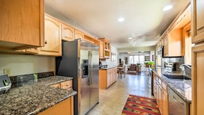 A kitchen with granite countertops, wooden cabinets, a refrigerator, and a patterned rug.