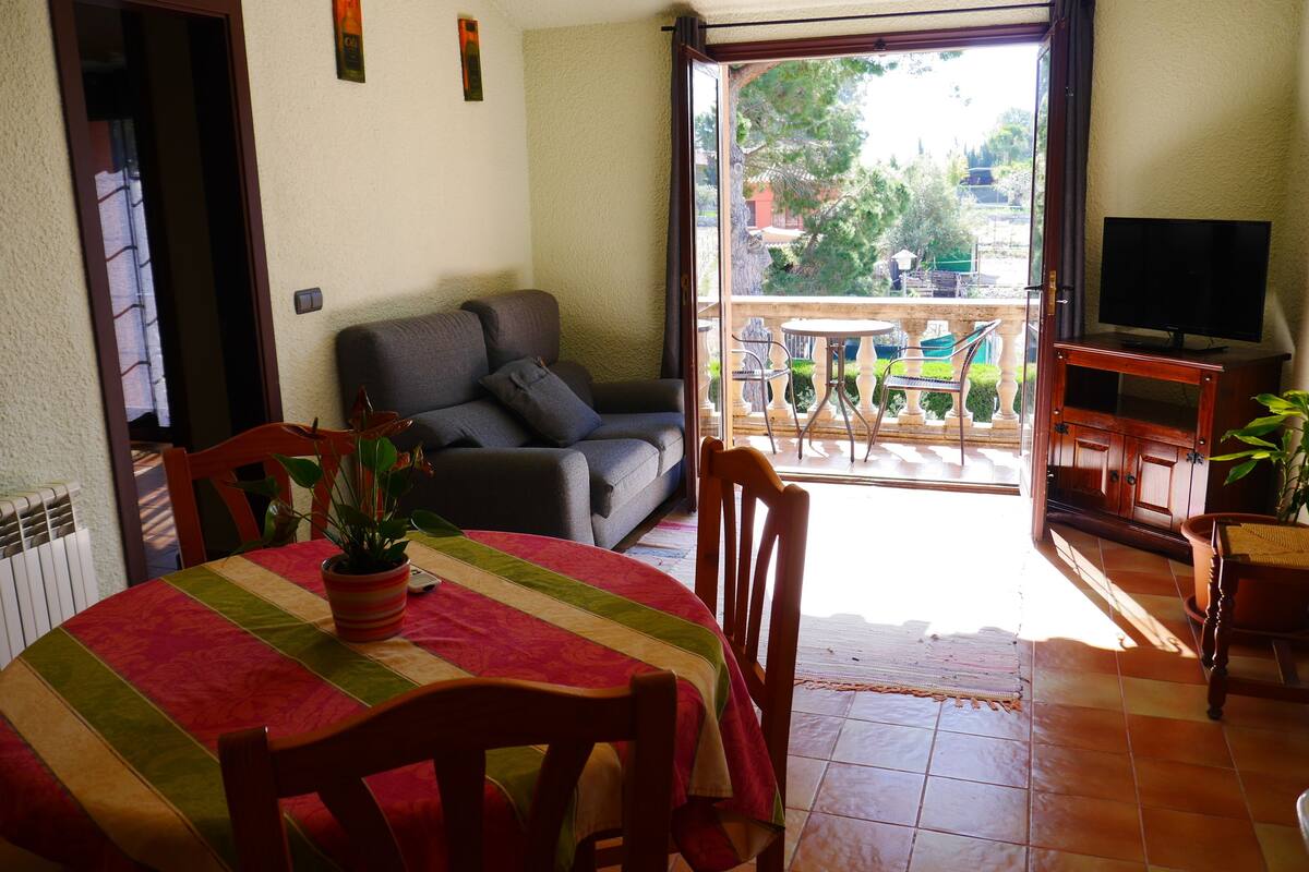 A living room with a sofa, a dining table with chairs, a TV stand, and a balcony with a table and chairs.