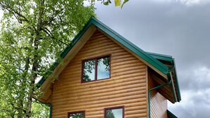 Eine zweistöckige Holzhütte mit Garage, umgeben von Bäumen.