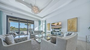 Ein geräumiges Wohnzimmer mit einem großen Glastisch, grauen Polstersofas und einem modernen Kronleuchter.