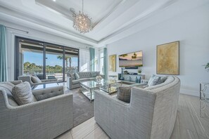 A spacious living room with a large glass coffee table, grey upholstered sofas, and a modern chandelier. - Bright Chic Oasis with Private Pool and Spa at Reunion (Kissimmee)