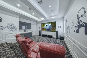 A modern home theater room with a large flat-screen TV, a leather reclining chair, and a patterned carpet.