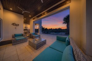 A modern outdoor seating area with wicker furniture and a glass coffee table, overlooking a pool and a sunset view. - 7BR Reunion Villa | Pool & Themed Kids Rooms (Kissimmee)
