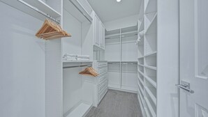 Ein begehbarer Kleiderschrank mit weißen Regalen, Holzaufhänger und einem grauen Teppich.