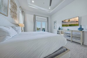 A bedroom with a large bed, a nightstand, a dresser, and a television on the wall.