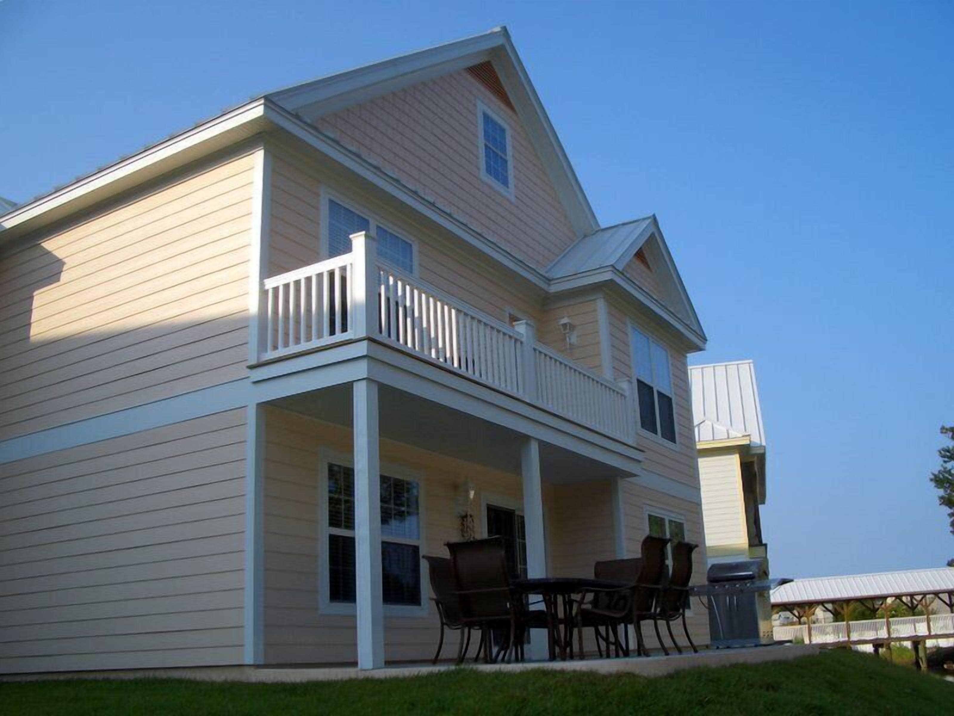A two-story house with a balcony and a patio area with outdoor furniture.