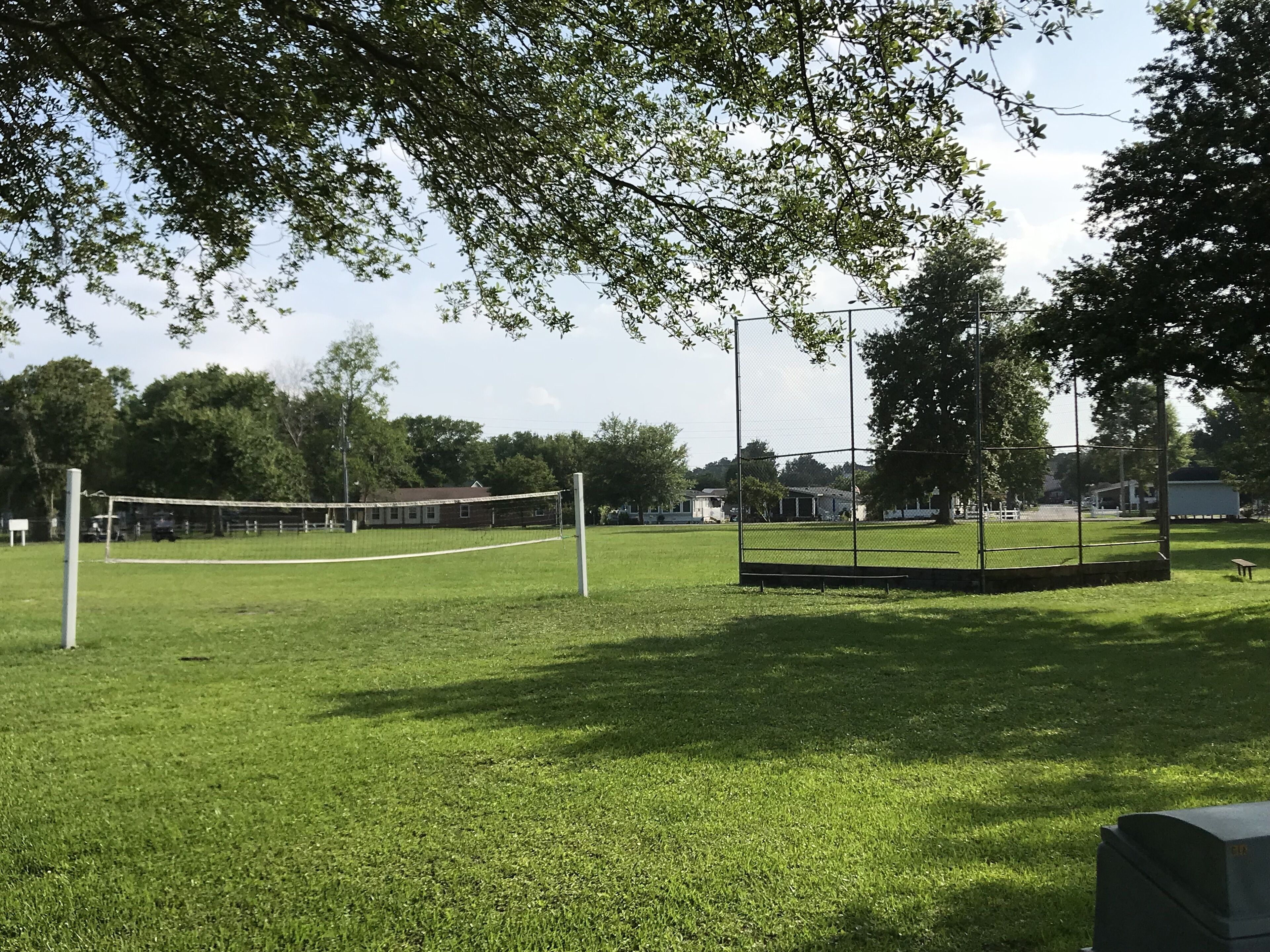 A grassy sports field with a volleyball net, surrounded by trees and a fence.