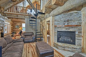A log cabin interior with a stone fireplace, leather sofas, and a spiral staircase. - Custom Log Cabin w/ Deck & 45 Acres By Pine River! (Tustin)