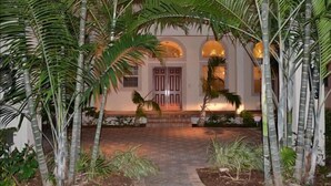 A building with a central entrance, surrounded by tall palm trees and a paved pathway leading to the door. - BY THE SEA VACATION VILLAS 5 BED WATERFRONT/ POOL LARGE ESTATE NEAR BEACH (Pompano Beach,)