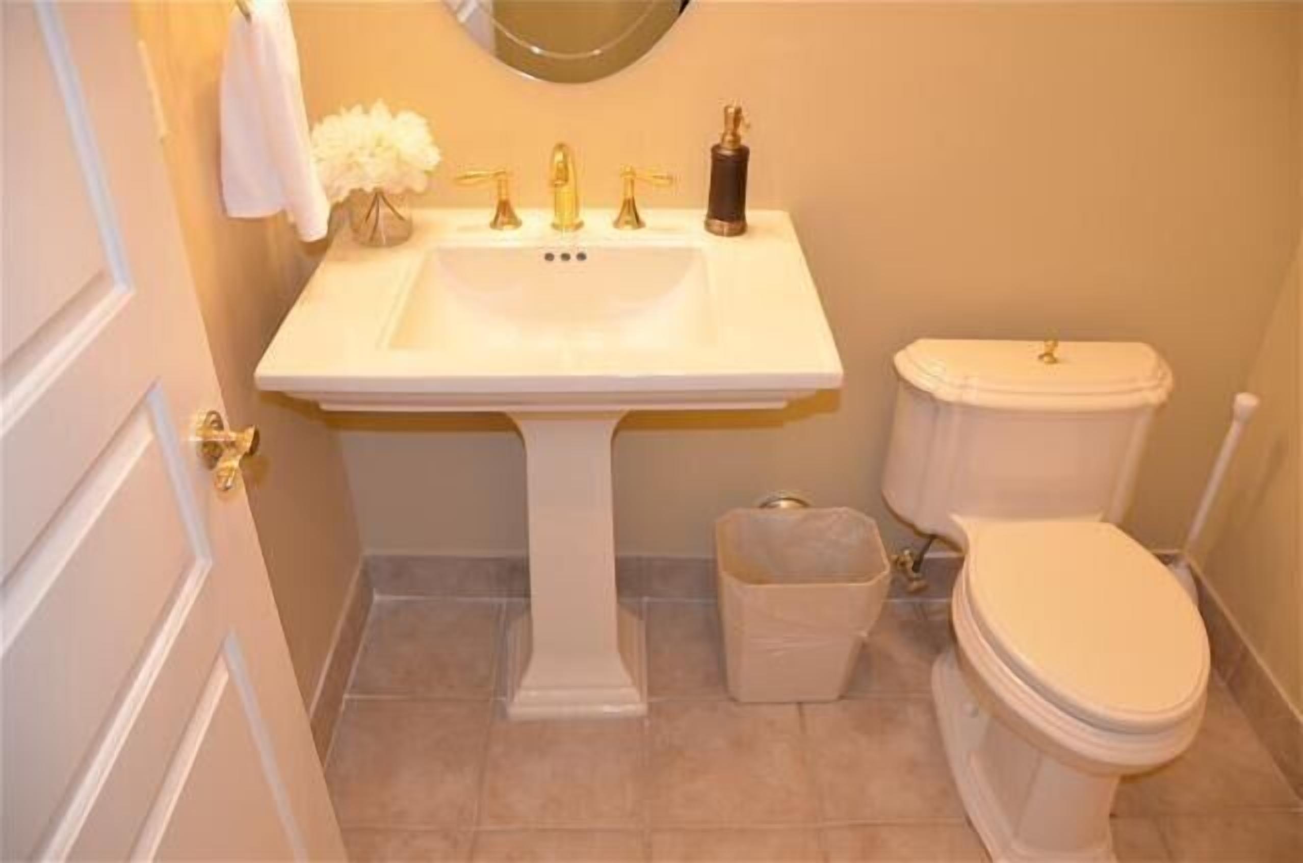 A bathroom with a pedestal sink, a toilet, and a trash bin.