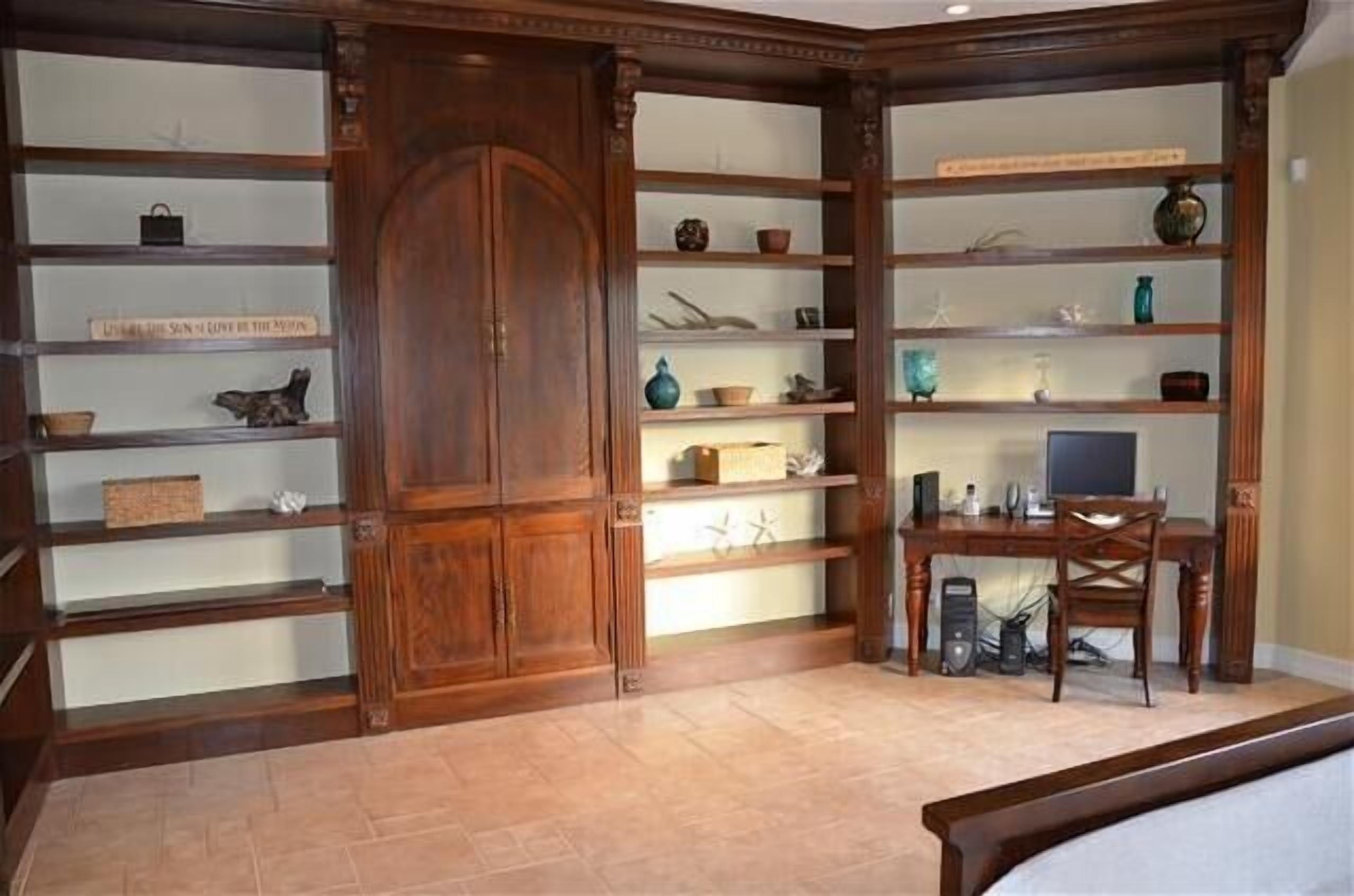 A room with wooden shelving units displaying various decorative items and a desk with a computer.