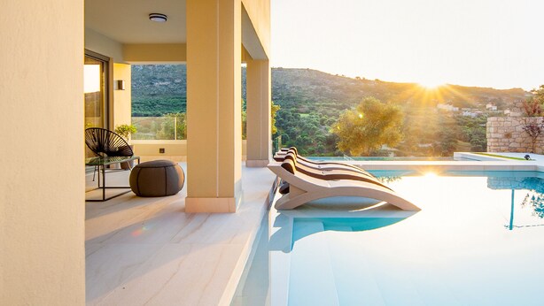 Ein moderner Poolbereich im Freien mit Blick auf die Landschaft, eine Sitzgruppe mit Tisch und Stühlen sowie ein architektonisches Design in sonnigem Licht.