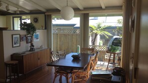 Un espace repas avec une table et des chaises en bois, un comptoir en bois doté d’un évier, et une vue sur l’extérieur à travers une clôture en bois.