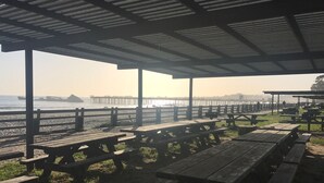 Un pavillon situé au bord de la plage, doté de bancs en bois et de tables de pique-nique, d’où l’on peut admirer l’océan et une jetée.