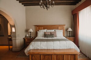 A bedroom with a wooden bed, two bedside tables with lamps, a chandelier, and an arched doorway.
