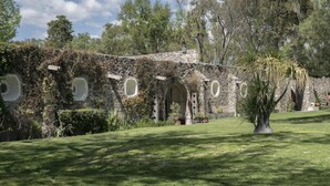 A stone building with circular windows and a garden in front. - Meson Real de la Plata (El Marques)