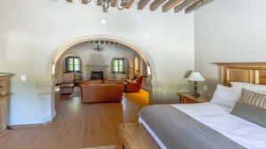 A bedroom with a large bed, a sofa, and a chair. There is a wooden floor and a chandelier. - Meson Real de la Plata (El Marques)