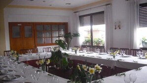 Un comedor con varias mesas dispuestas para una comida, con manteles blancos, platos y copas de vino.
