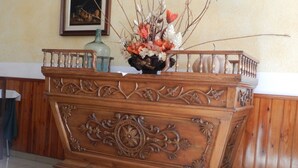 Un mostrador de recepción de madera con intrincados grabados, un florero con flores y un cuadro en la pared.