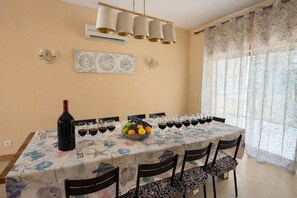 Een eetkamer met een lange tafel, stoelen, een wijnfles, glazen en een schaal fruit.